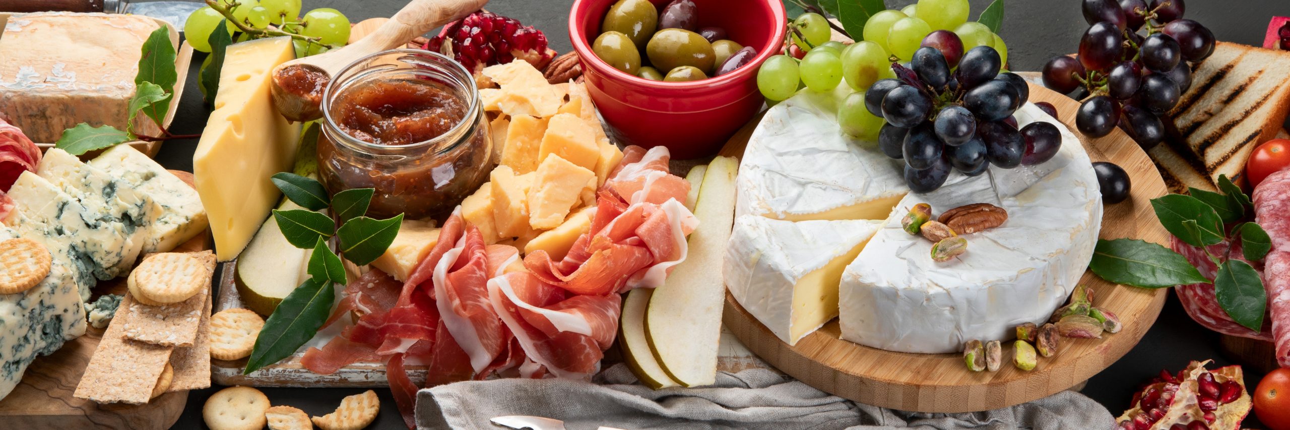 Appetizers table. Cheese, fuits and meat board on dark  background. Panorama banner