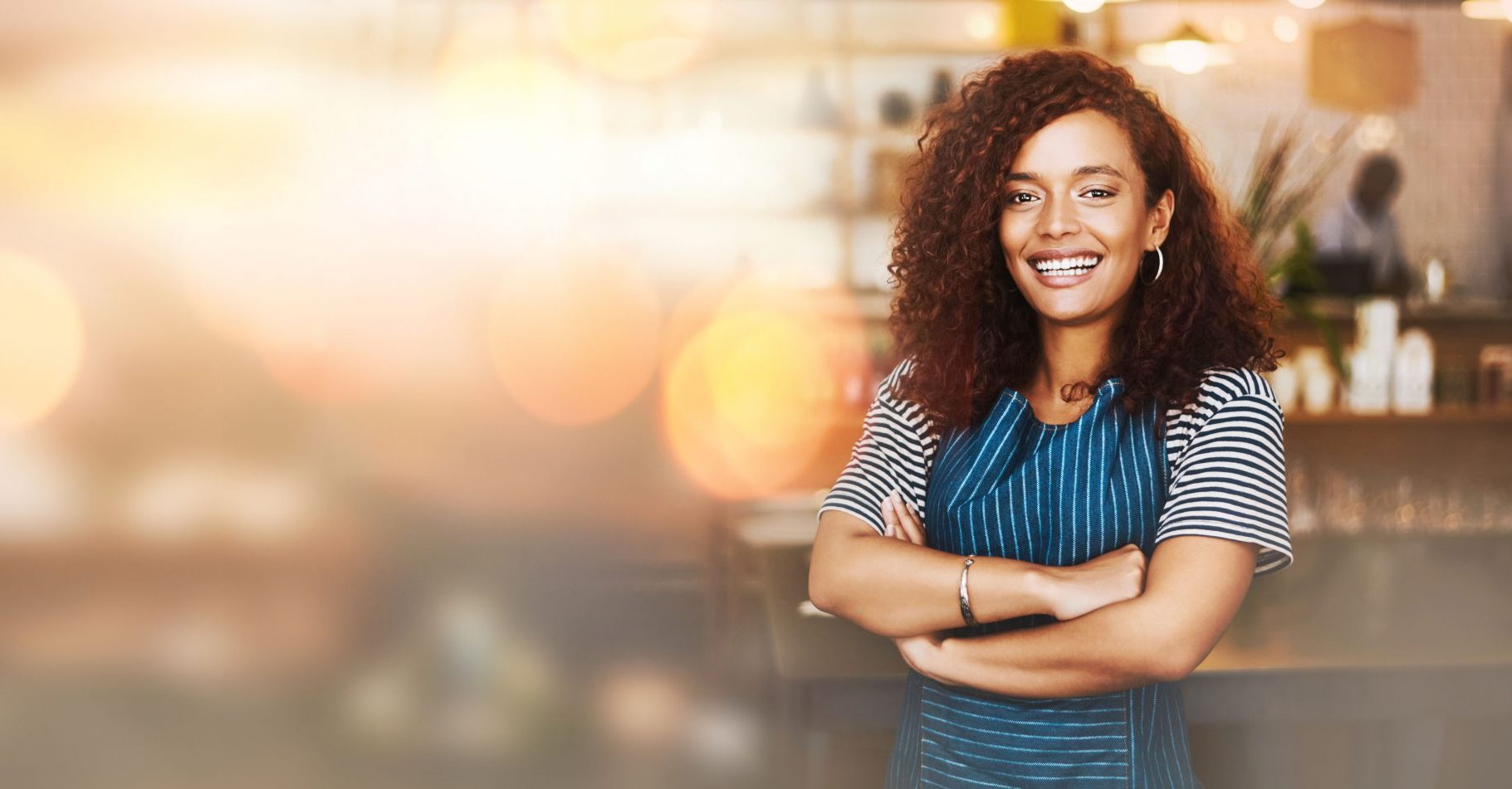 Black woman, portrait and barista with arms crossed on bokeh and smile in small business at coffee shop. Happy African American female entrepreneur or waitress smiling in management on mockup at cafe.